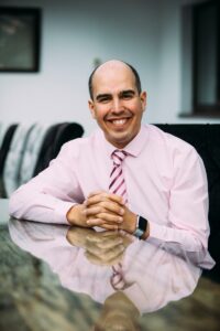 Prof Adam Boddison OBE siting at a desk and smiling
